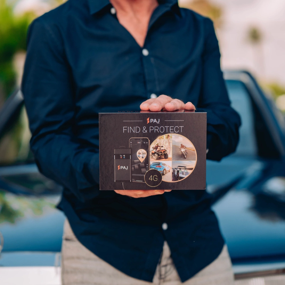 A man in blue shirt infront of his black car holding vehicle finder 4g gps tracker box.